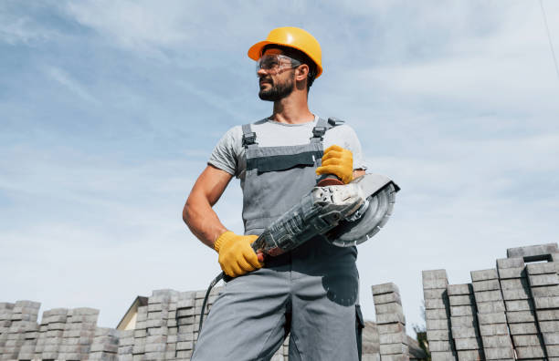 Posing for a camera with circular saw. Male worker in yellow colored uniform have job with pavement stock photo