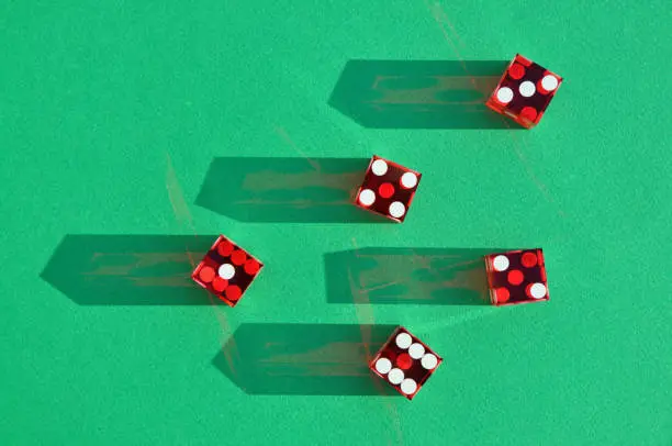 Photo of Red Casino or craps dice on green baize surface. Sunlit shadow