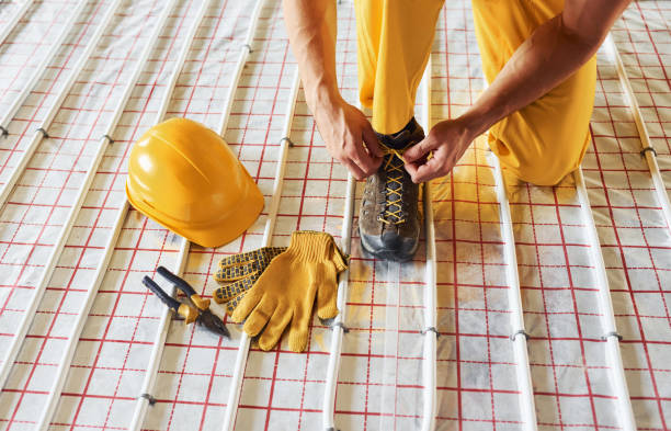 istock Sits and wears shoes. Worker in yellow colored uniform installing underfloor heating system 1330878821
