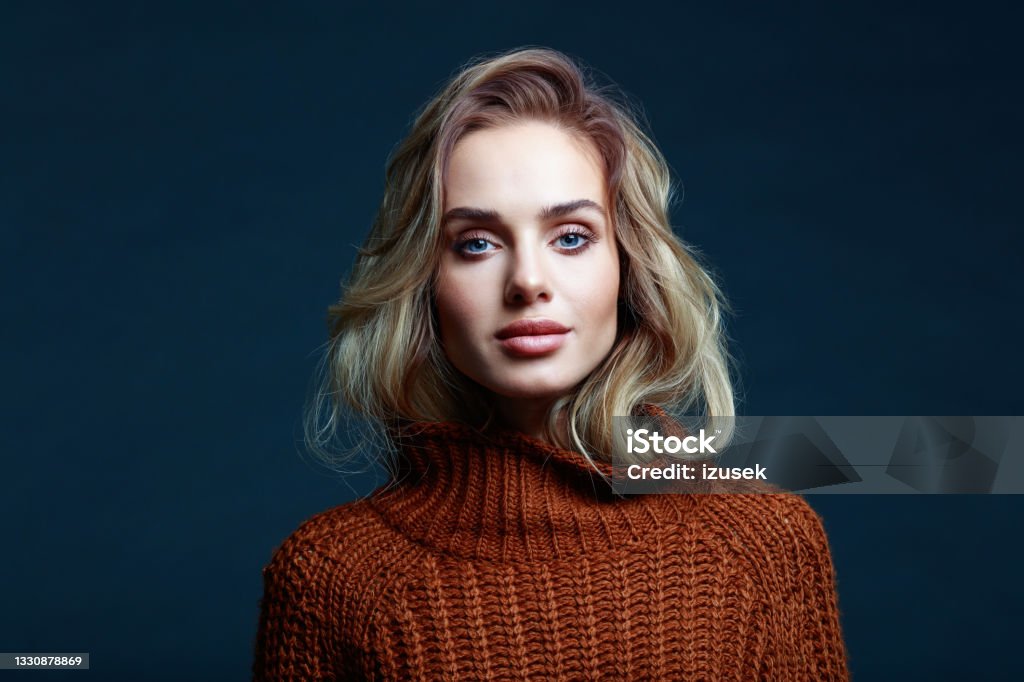 Fashion portrait of beautiful woman in brown clothes, dark background Portrait of long hair blond young woman wearing brown sweater, looking at camera. Studio shot against black background. Women Stock Photo