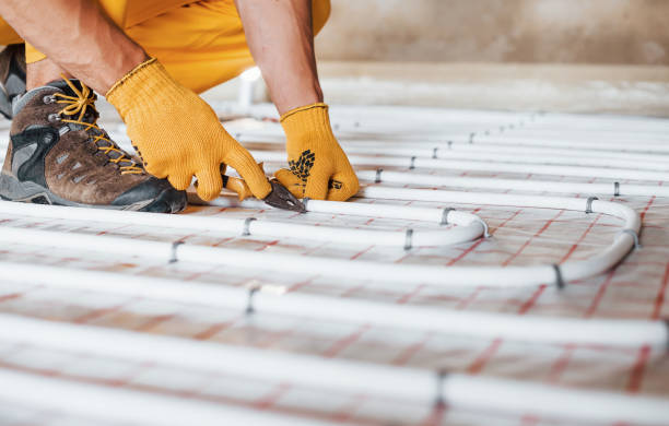 Close up view. Worker in yellow colored uniform installing underfloor heating system stock photo