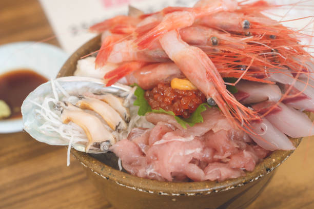 A big bowl of seafood rice topped with a large amount of sashimi, including hokki-gai from Tomakomai, Hokkaido, sweet shrimp, mushi-ko scallops, etc. stock photo