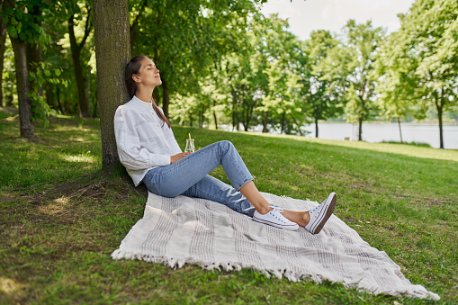 Young woman resting in park sitting on picnic blanket