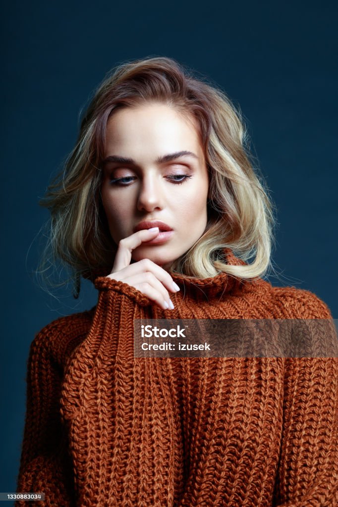 Fashion portrait of woman in brown clothes, dark background Portrait of long hair blond young woman wearing brown sweater, looking down. Studio shot against black background. One Woman Only Stock Photo