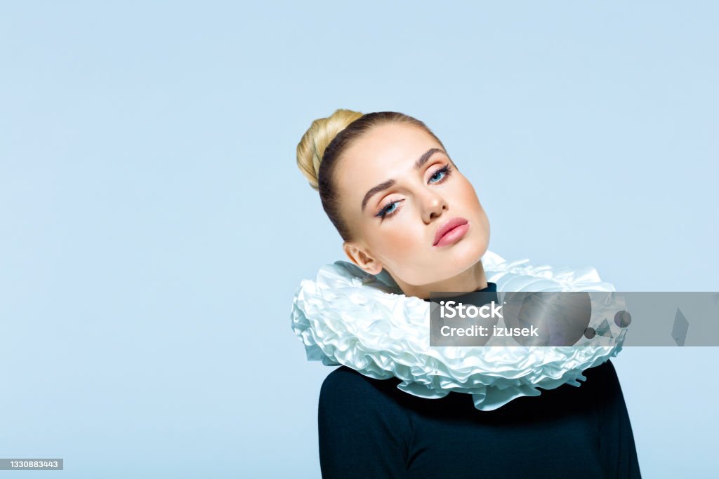 Portrait of woman wearing neck ruff Woman wearing black turtleneck and white neck ruff looking at camera. Studio shot on blue background. Neck Ruff Stock Photo