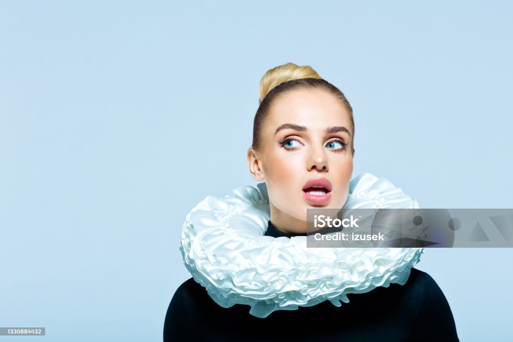 Portrait of woman wearing neck ruff Surprised woman wearing black turtleneck and white neck ruff looking away. Studio shot on blue background. Neck Ruff Stock Photo