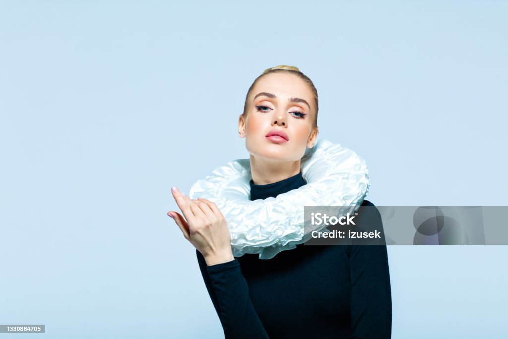 Portrait of woman wearing neck ruff Woman wearing black turtleneck and white neck ruff looking at camera. Studio shot on blue background. Actress Stock Photo