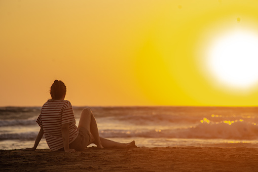 Woman is sitting on the beach and looking at the sea