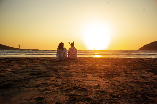 Two female friends are on the beach, they are looking at the sea and sunset