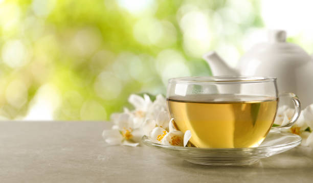 istock Cup of jasmine tea and fresh flowers on grey table outdoors, space for text. Banner design 1330890773