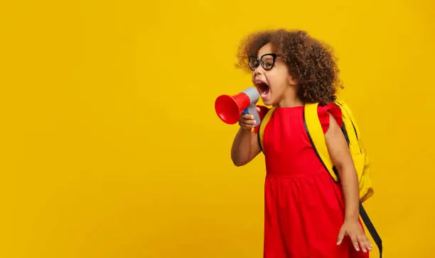 Photo of Little cute Black girl in red dress holding in hand and speaking in electronic gray megaphone