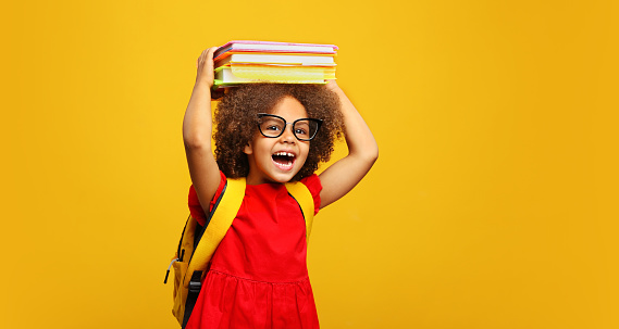 divertida niña negra sonriente de la escuela con gafas sostiene libros en su cabeza photo