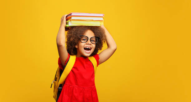 drôle souriante enfant noire de l’école avec des lunettes tenir des livres sur sa tête - élève photos et images de collection
