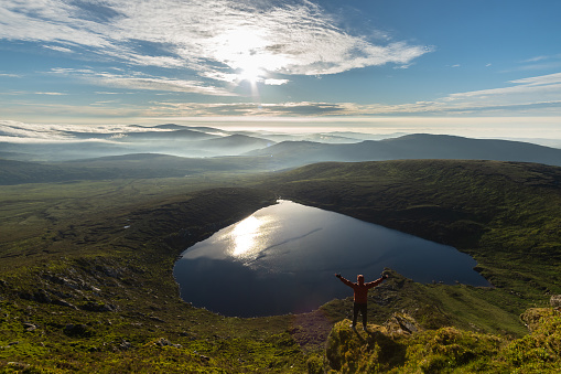 Man raising his arms to the air on top of mountain in Lough Ouler County of Wicklow Ireland