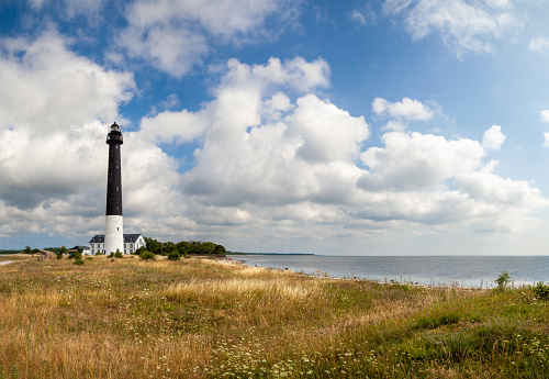 The Sorve lighthouse on the island Saaremaa in Estonia surrounded with orange grass land under cloudy blue sky in summer day.