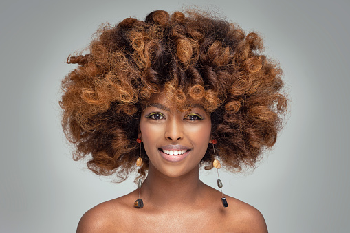 Beauty portrait of happy afro american woman with culry hairstyle and glamour colorful makeup. Girl wearing fashionable boho earrings. Studio shot.