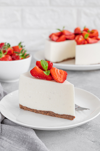 No baked cheesecake with fresh strawberries and mint on top on a white plate on a gray concrete background. Copy space