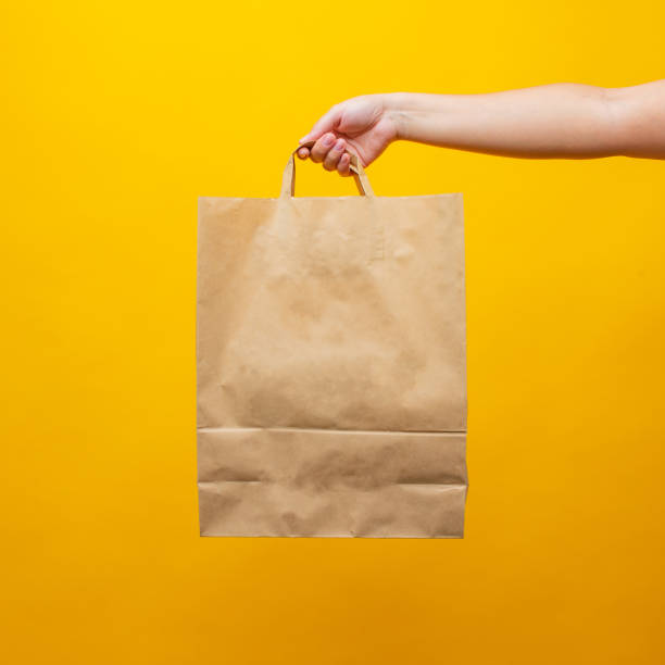 istock A woman's hand with an paper bag on a yellow background 1330894484