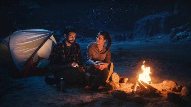 Happy Couple Nature Camping in the Canyon at Night, Use Digital Tablet Computer, Sitting by Campfire. Two people Have Fun, Smile, Post Traveling Photos on Social Media, Watch Funny Videos on Internet feliz pareja naturaleza acampar en el cañón por la noche, utilizar la tableta digital de ordenador, sentado junto a la fogata. dos personas se divierten, sonríen, publican fotos de viaje en las redes sociales, ven videos divertidos en internet