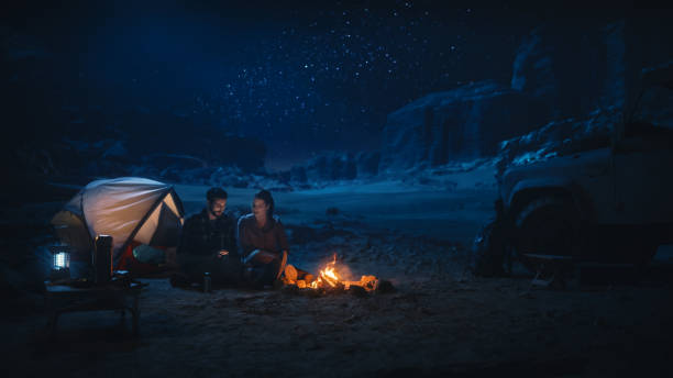 istock Happy Couple Camping in the Canyon at Night, Use Digital Tablet Computer, Sitting by Campfire. Two people Have Fun, Smile, Post Traveling Photos on Social Media, Watch Funny Videos on Internet 1330897066
