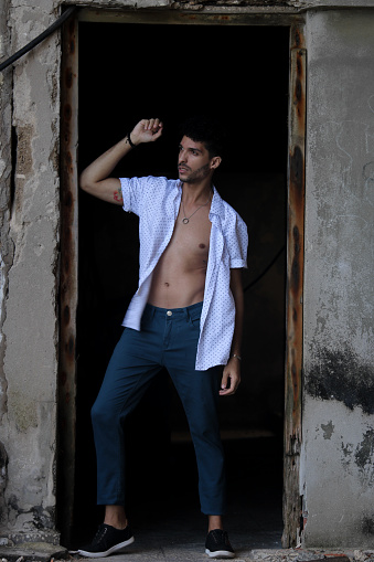 A young Latino model has his shirt open and poses for a photo. The young man is happy and looks into the camera