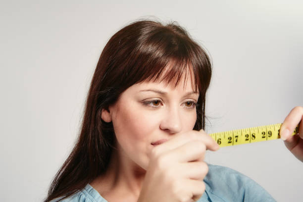 istock Checking on diet progress, beautiful young woman examines a yellow tape measure 1330901341