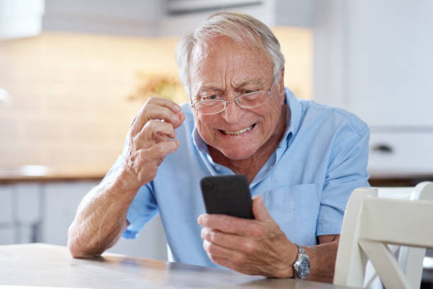 Shot of an elderly man using his cellphone at the kitchen table at home Remember me when you're the one you've always dreamed phone spam photos stock pictures, royalty-free photos & images