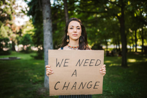 「私たちは変化が必要」ポスターを持つ若い活動家/抗議者 - sign protestor protest holding ストックフォトと画像