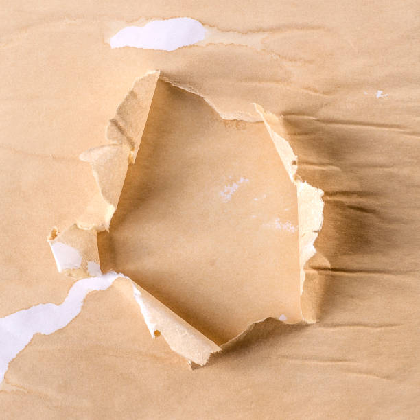 istock Horizontal background with a torn hole in torn coffee-colored paper. Background with beige hole in aged paper. 1330905183