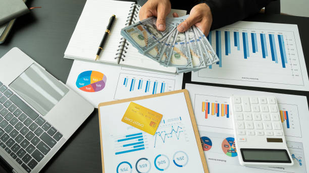 istock Female accountant using calculator and computer holding pen with financial graph and calculate home office expenses on top view table. 1330905884