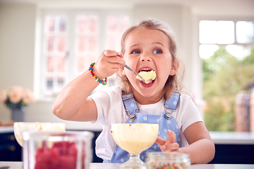 Young Girl In Kitchen Eating Ice Cream Dessert With Spoon