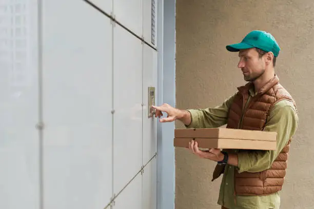 Side view portrait of delivery man holding pizza and ringing doorbell, copy space