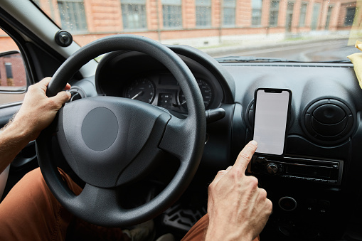 Close up of unrecognizable man driving car focus on hand tapping at smartphone with blank screen, copy space