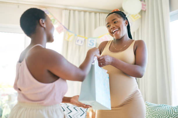 foto de una mujer dándole a su amiga un regalo en su baby shower - baby shower women home interior indoors fotografías e imágenes de stock