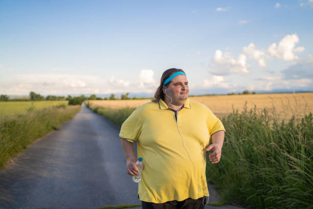 uomo in sovrappeso che fa jogging mentre ascolta musica - loose weight foto e immagini stock