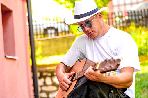 Stock photography of a mature man playing a guitar outside of his home and enjoying the beautiful melody. Chilling in a sunny day, fresh air and positive energy.