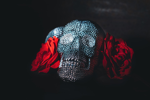 Shiny sparkling bright skull candy with red rose and a disco ball. Party invitation for Halloween. Close up, selective focus.