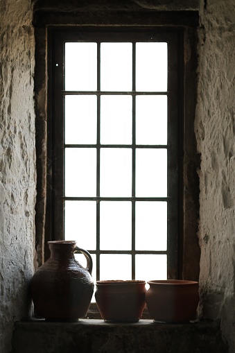 An old leaded house window with small oblong ￼ glass pane￼￼s silhouette still life silhouetted jug and two bowls ￼￼on a stone windowsill