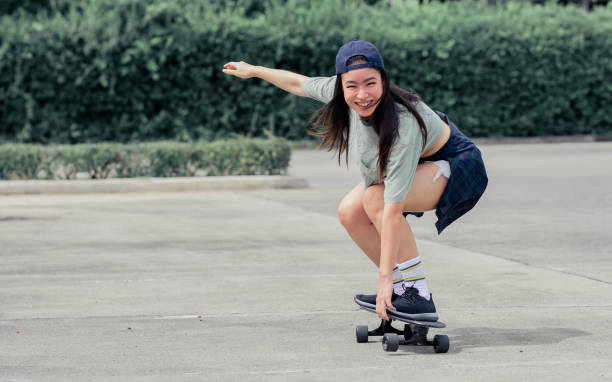 porträt schöne sportliche asiatische skaterin im hipster-shirt mit shorts, lächelt vor glück, steht auf skateboard und spielt draußen mit kopierraum. aktivitäts- und abenteuerkonzept. - skateboard skateboarding outdoors sports equipment stock-fotos und bilder