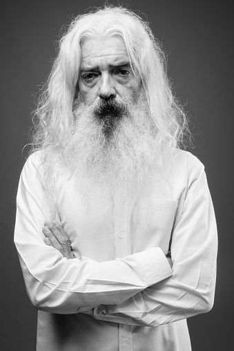 Studio shot of senior man with long hair and beard against gray background in black and white