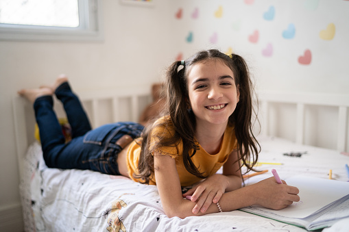 Portrait of girl lying on bed writing on note pad or dairy at home