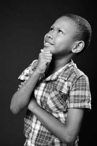Isolated on white. Little African boy making a facial expression. Here he is pointing a finger to his head thinking.