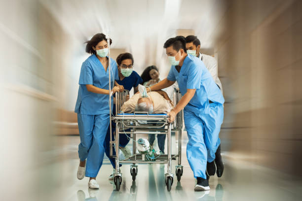 emergency department: group of doctors, nurses, paramedics push gurney, stretcher with seriously trauma patient towards the operating room. group of asian staff rushing to save the people live in the hospital - urgent imagens e fotografias de stock