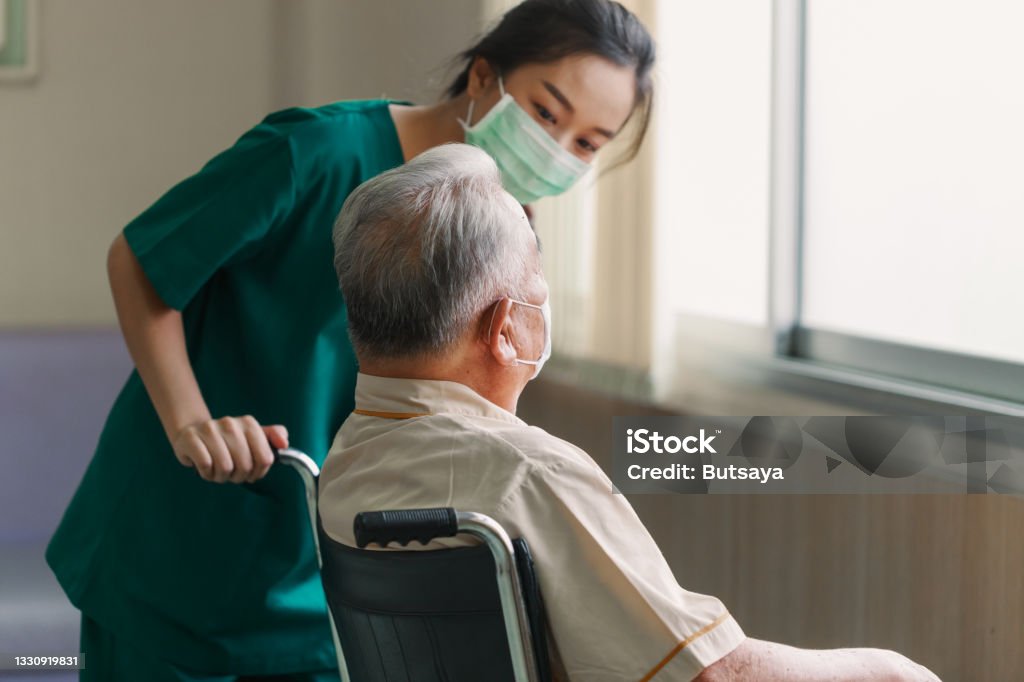 Young Asian woman nurse explaining information to elderly man patient in wheelchair with friendly smiley face in the hospital. Young Assistance with old people in the elderly care place Young Asian woman nurse explaining information to elderly man patient in wheelchair with friendly smiley face in the hospital. Young Assistance with old people in the elderly care place. Nursing Home Stock Photo