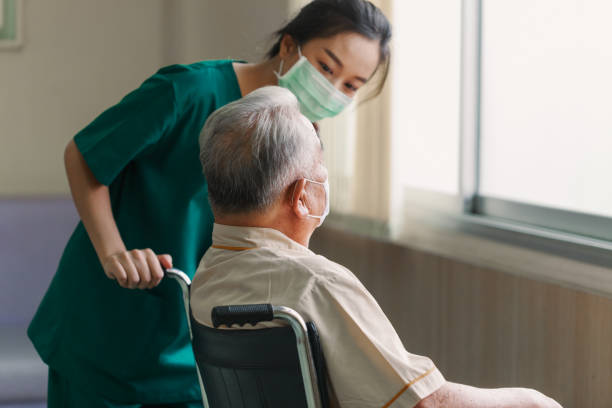 молодая азиатская женщина-медсестра объясняет информацию пожилому мужчине в инвалидной коляске с дружелюбным улыбающимся лицом в больниц - civilian стоковые фото и изображения
