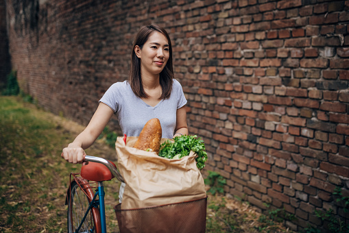 One woman, female Japanese pushing a bicycle with a bag with vegetable groceries, she is in going home.