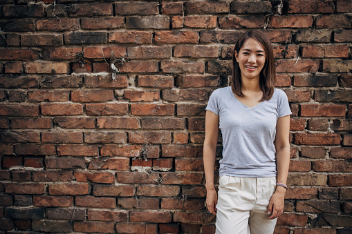 One woman, portrait of a beautiful Japanese woman standing by a brick wall outdoors.