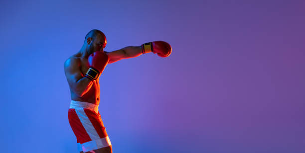 istock One professional boxer in red shorts training, exercising over purple background in neon light. Side view 1330922266