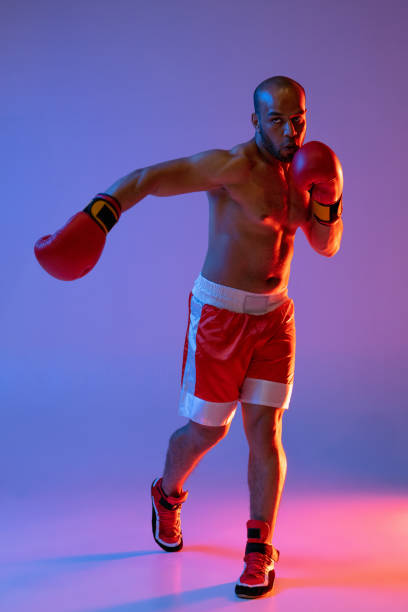 istock Vertical image of one professional boxer in red shorts training, exercising isolated over purple background in neon light. 1330922331