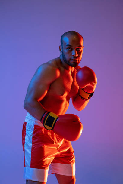 istock Vertical image of one professional boxer in red gloves training, exercising isolated over purple background in neon light. 1330922336
